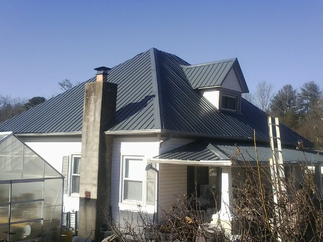 Dark blue standing seam metal roof on a white farmhouse with dormer — Slate & Tile Roof Repair by Roofing Brothers in Spring