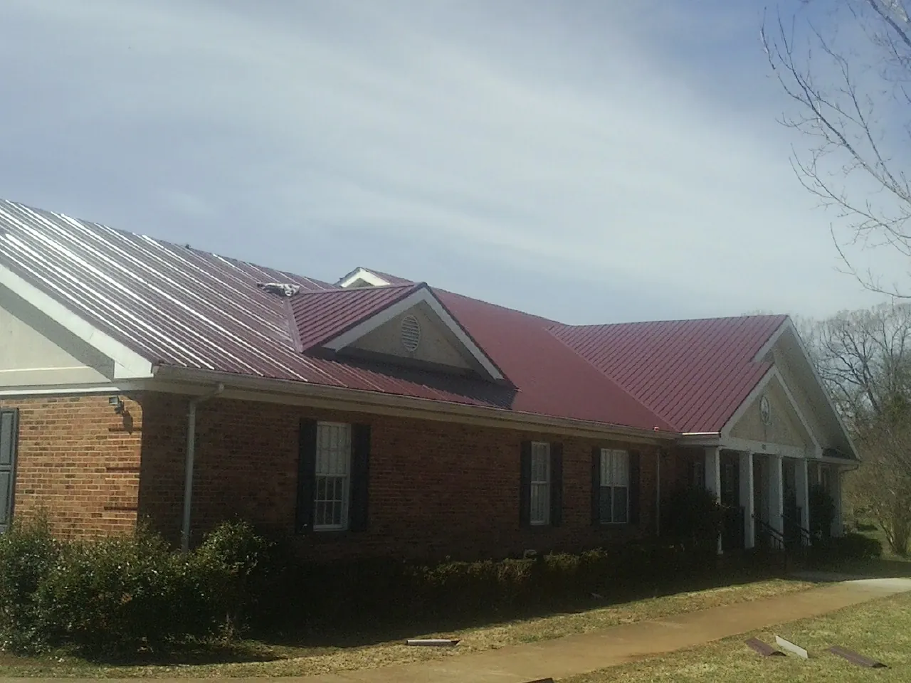 Red metal roof with gabled entries on a long brick building, from a Hail Damage Roof Repair job in Spring