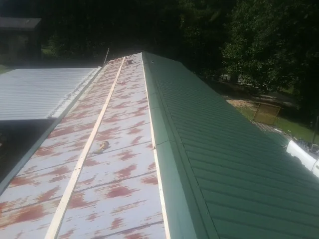 Old rusted panels beside newly installed green metal roofing — Wind Damage Roof Repair by Roofing Brothers in Spring