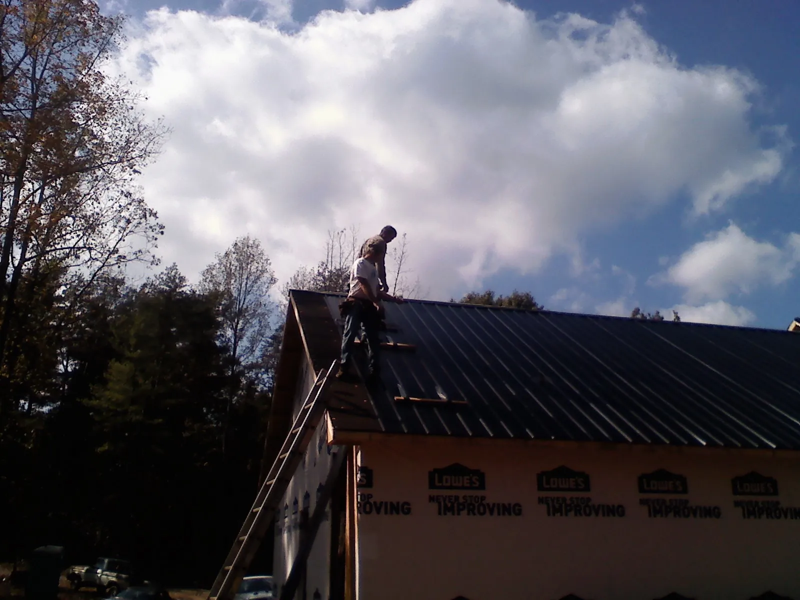 Roofer fastening dark metal panels high against a cloudy sky, from a Roof Inspection job in Spring
